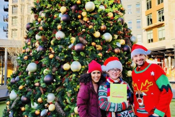 Three people in festive clothing standing in front of a Christmas tree