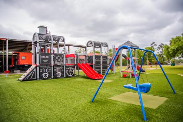 railroad themed playground with a model train, slide, and swing set