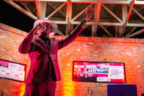 singer wearing a purple suit and white hand stands on arcade ampitheater stage with live at the lakefront sign in the back