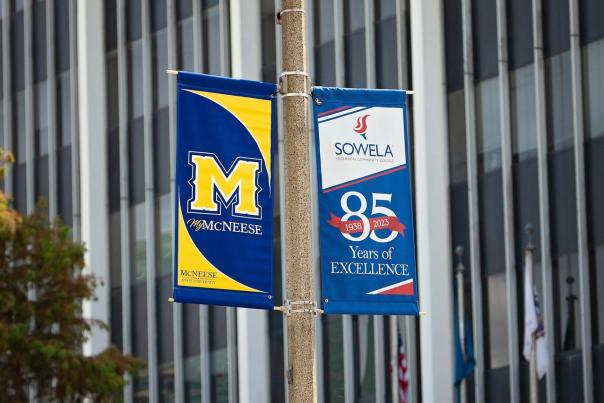 blue and gold mcneese state university flag and white, blue and red sowela flag celebrating 85 years of excellence