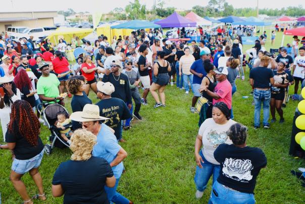 a crowd gathers outside dancing on the grass. tents and covers can be seen in the background and sound equuipment