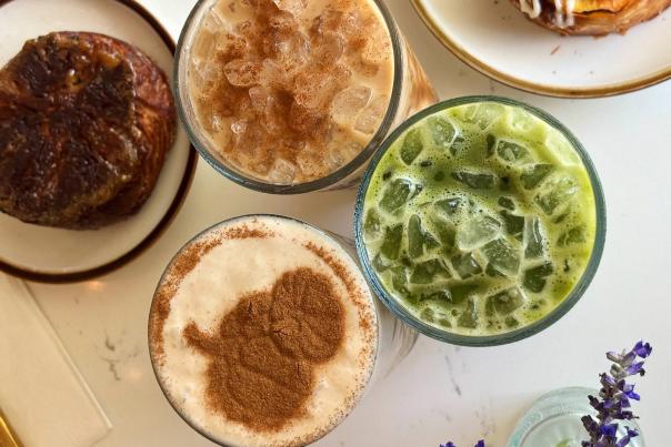 overhead shot of fall drinks and pastries at the bekery, one is an iced green drink, one is an iced latte, one has pumpkin cinnamon