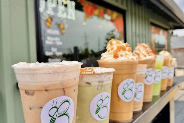 eight frozen coffee beverages are lined up on a porch with a green B for the Buzz logo