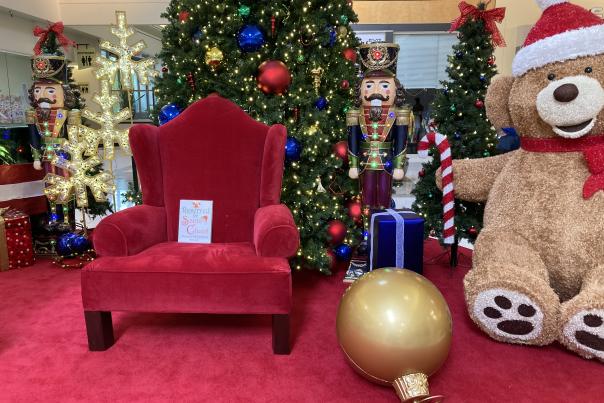 An empty red arm chair reserved for Santa with Christmas tree and nutcrackers and large ornament and bear stage set.