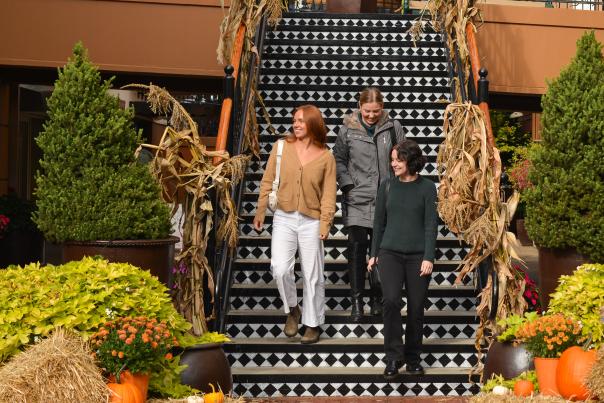 Three people walk down steps in an outdoor shopping mall decorated with haybales and pumpkins.