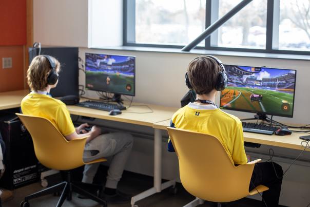 Two student competing in the MHSEL Esports Championships, each facing their own monitor and wearing headphones.