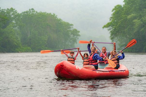 Family holds rafting paddles above their head while floating on a white water raft