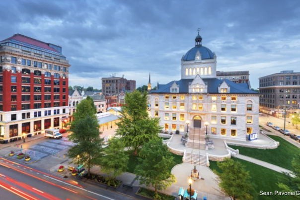 Overcast sky with tall red building and old courthouse with a blue roof illuminated by light
