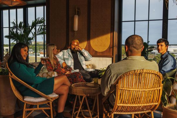 People gathered around a table with big windows and blue sky at Lost Palm the rooftop bar and eating area in the Manchester Hotel in Lexington, Ky.