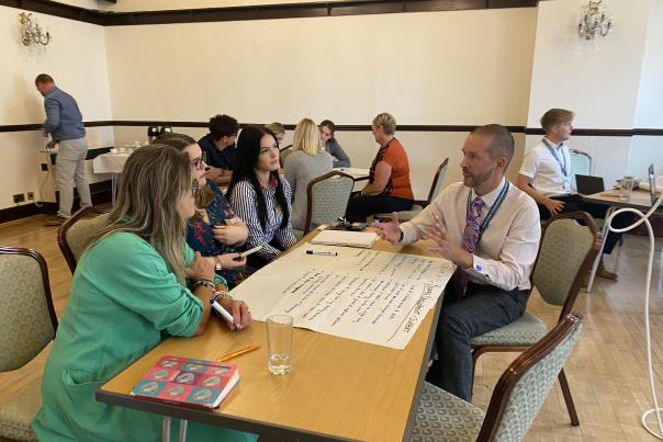 A group of people sit around a table with a whiteboard in a conference venue