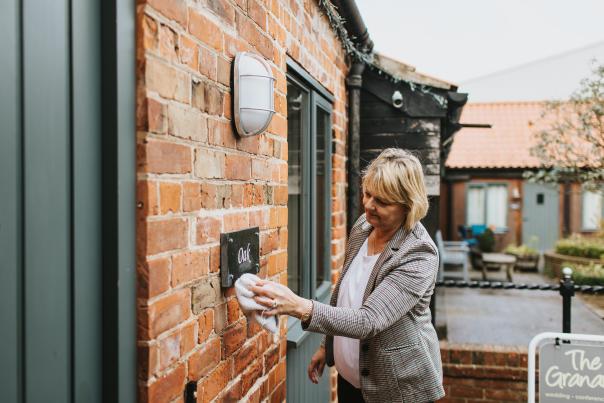 A woman wiping a plaque on a cottage in a courtyard.