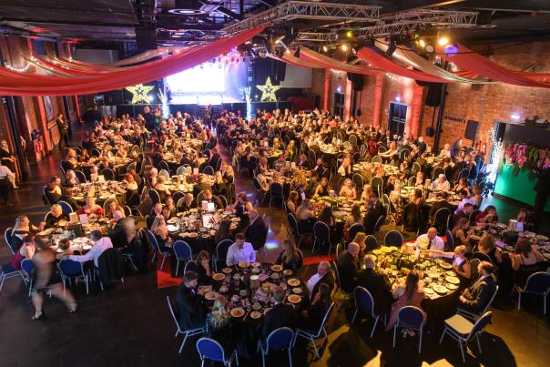 An event hall filled with people at tables and a stage in the distance.
