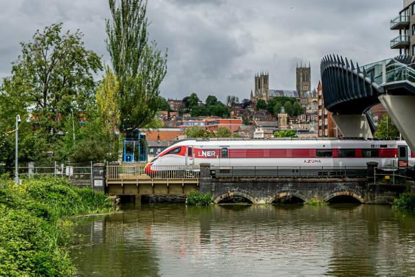a train going across a bridge with a river underneath and a cathedral in the background