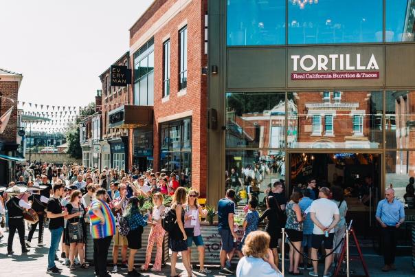 A queue of people on a sunny day outside the fast food restaurant 'Tortilla'