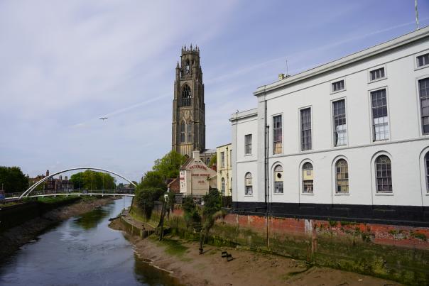 A view of Boston Stump with the River Witham in the foreground, blue skies overhead