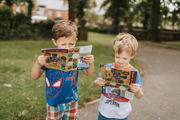 Two young boys holding treasure trail maps in a park in Lincoln