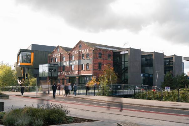 a old brick library building under cloudy sky with students walking in the foreground
