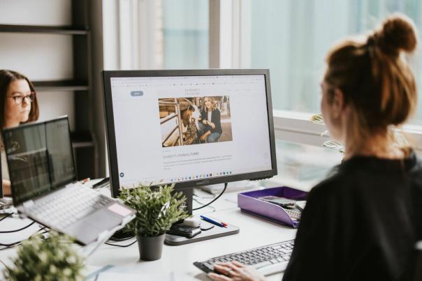 A woman looking at a website on a monitor sat at a desk in an office