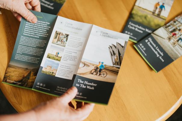 a person holding a cycle Lincolnshire route brochure on top of a table