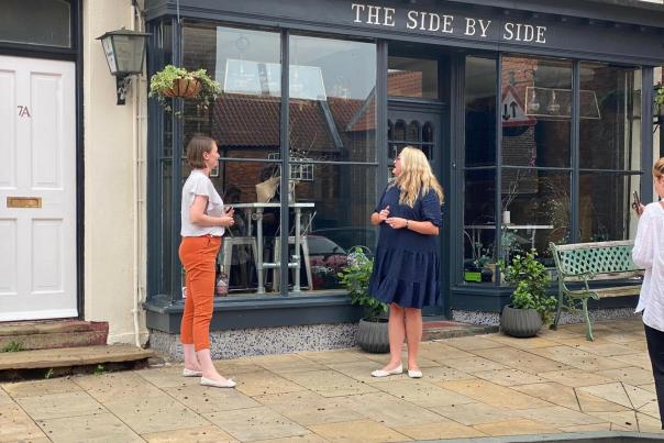 Two women standing outside a shop speaking business.