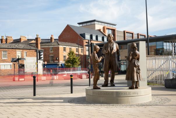 A statue of George Boole, showing him teaching two children, outside Lincoln Train Station
