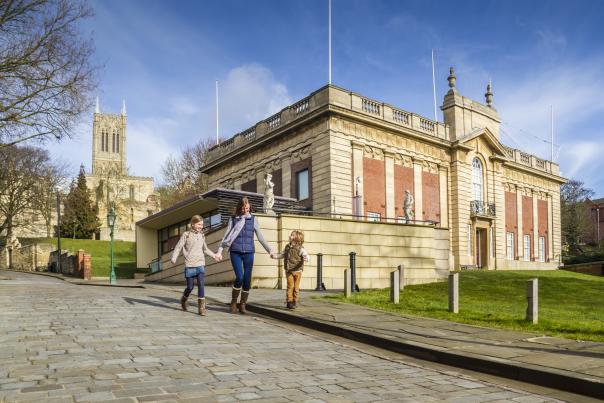 A family walking past the Usher Gallery with Lincoln Cathedral in the background