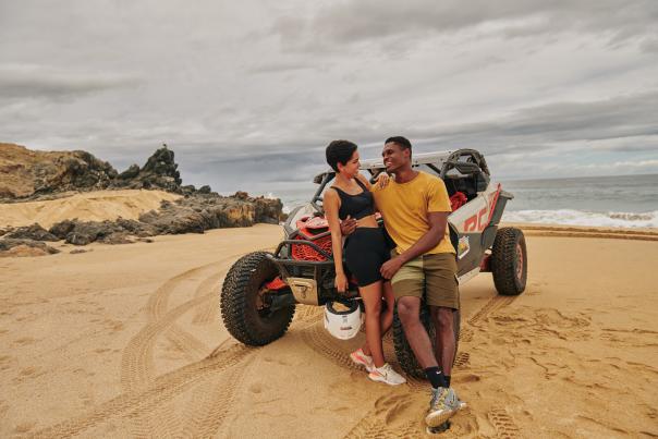 couple leaning on atv in the sand with the ocean behind them
