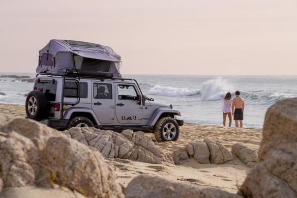 pareja frente a la costa en los cabos con una jeep tras ellos