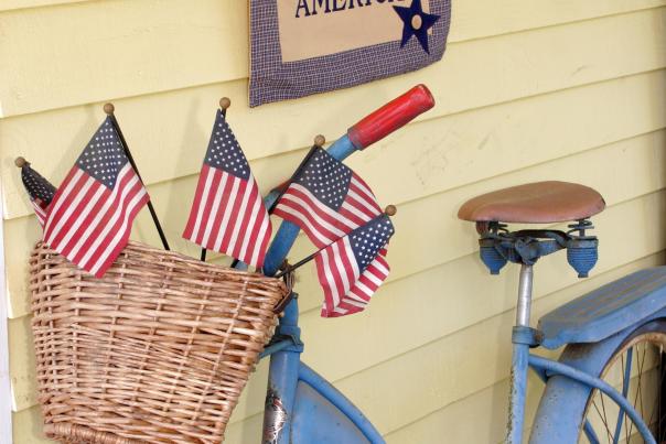 Vintage blue bicycle with American flags in a wicker basket below a God Bless America banner on a porch in Loudoun County VA
