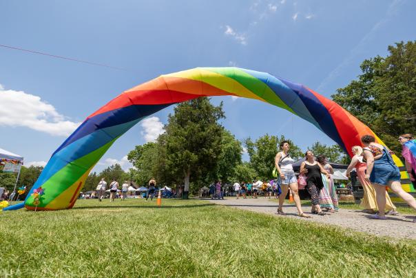 Attendees walk under a large rainbow arch at an outdoor Pride festival in Loudoun County, Virginia