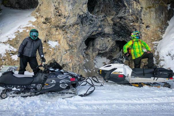 Two snowmobilers stand by their sleds in front of Devil’s Kitchen on Mackinac Island