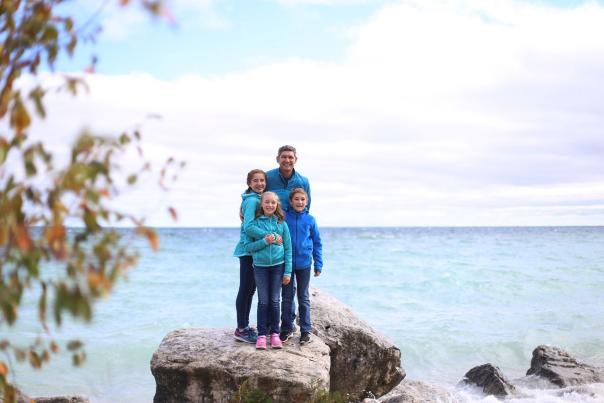 Family of four with two pre-teen tween children stands on a rock along Mackinac Island lakeshore