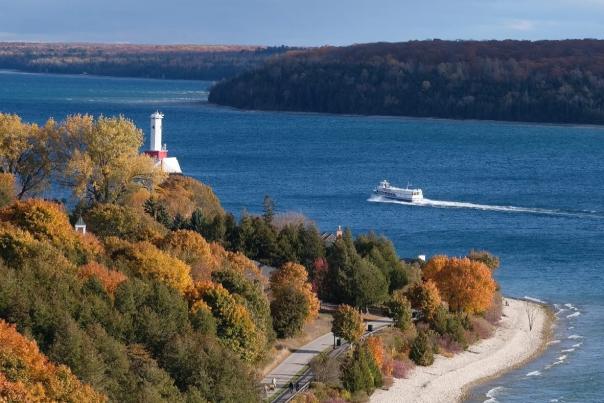Aerial view of Mackinac Island ferry boat nearing a lighthouse on a fall day with changing leaves