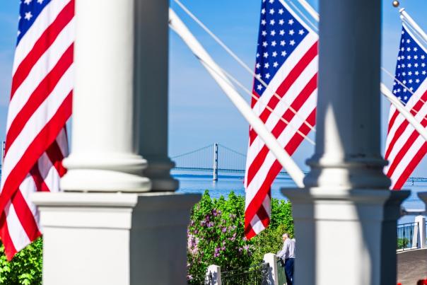 Mackinac Bridge framed by American flags and pillars on the porch of Mackinac Island’s Grand Hotel