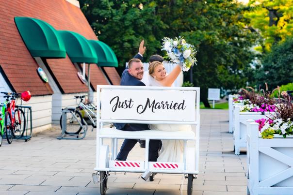 Bride and groom smile at camera while riding in a ‘Just Married’ rickshaw on Mackinac Island