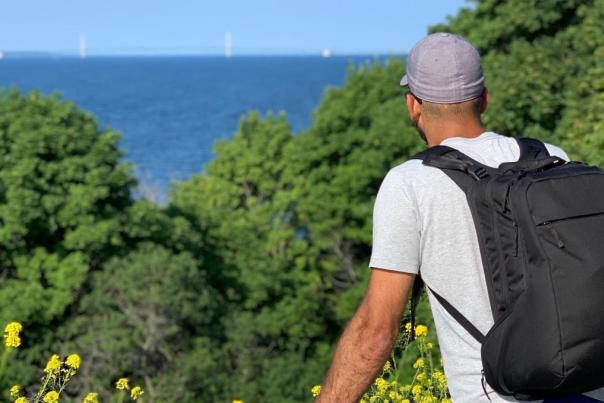 A man wearing a baseball cap and backpack looks out over the water at the Mackinac Bridge