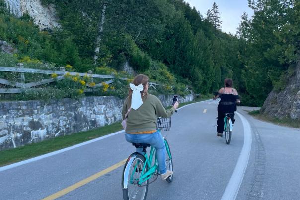 Two women ride bicycles along the road on car-free Mackinac Island