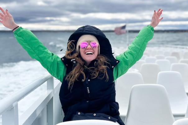 A smiling woman raises her hands to the sky on the top deck of a Mackinac Island ferry boat