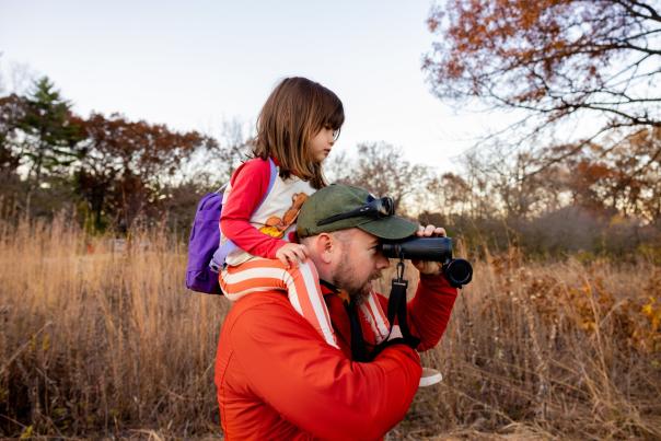 A small girl sits on a man's shoulders while he looks through binoculars at Governor Dodge State Park
