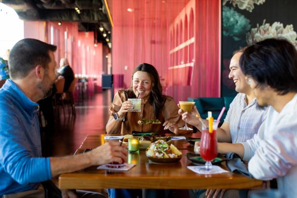An image of four people sitting around a table and chatting with cocktails and appetizers on the table in front of them.