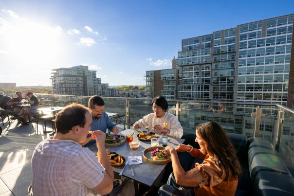 A group of friends enjoy their food while dining on a rooftop restaurant's outdoor patio.