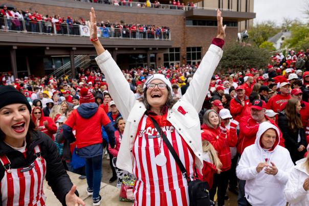 A white woman excitedly holds up her arms at a Badger tailgate