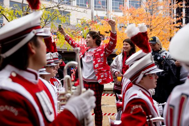 A man with brown hair cheers as the UW Madison marching band walks by.