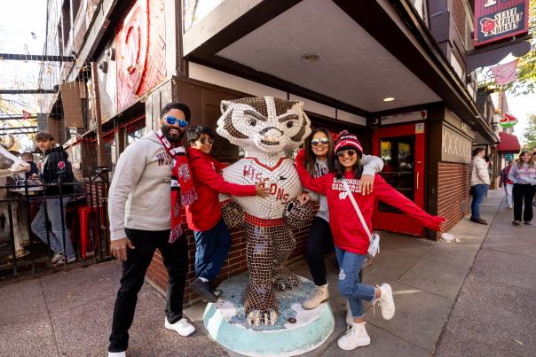 Family dressed in Badger gear poses next to Bucky Badger statue.