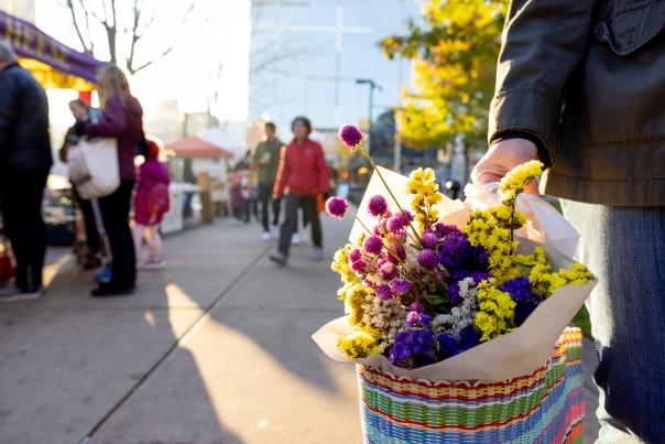 An image of a person carrying fresh flowers in a tote bag while walking around the Dane County Farmers' Market