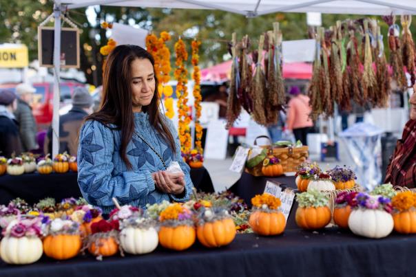 A woman looks at a table of flower arrangements made inside of small pumpkins at the Dane County Farmers' Market