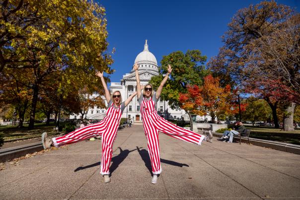 Two women wearing red and white striped overalls posing in front of the Wisconsin State Capitol building.