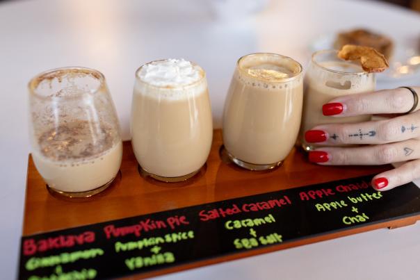 A coffee flight with four small coffee cups sitting on a flight each with a seasonal flavor including baklava, pumpkin pie, salted caramel and apple chaider