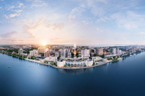 A panoramic view of a vibrant city skyline along a waterfront at sunrise, showcasing modern buildings and lush greenery.
