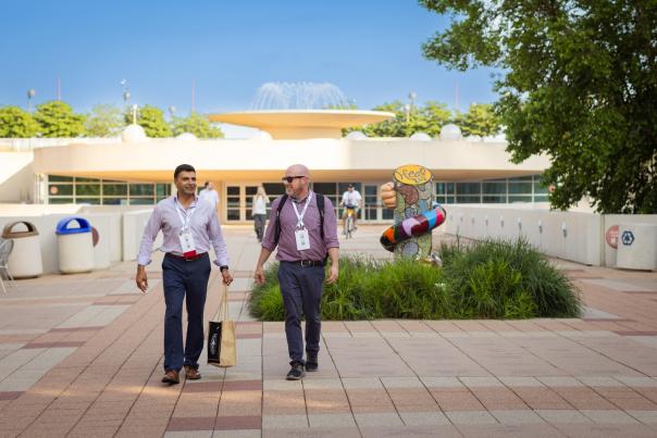 Two men dressed in business clothes walk from a STEM conference at the Monona Terrace Community and Convention Center with a fountain in the background.